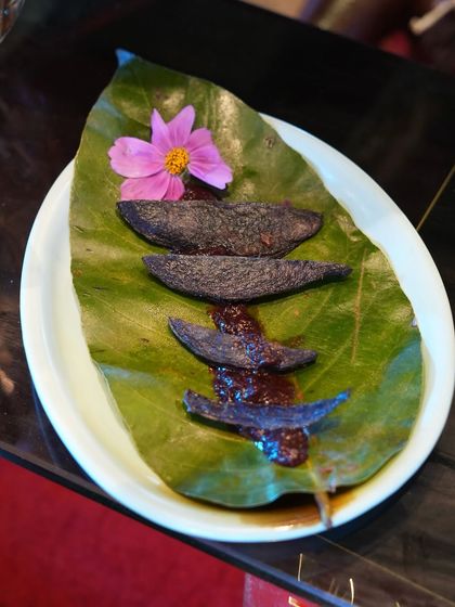 An artistic presentation of a unique dish featuring purple-hued elements on a bed of rich sauce, served on a natural leaf. This highlights our flair for creating visually intriguing and unconventional menu items.