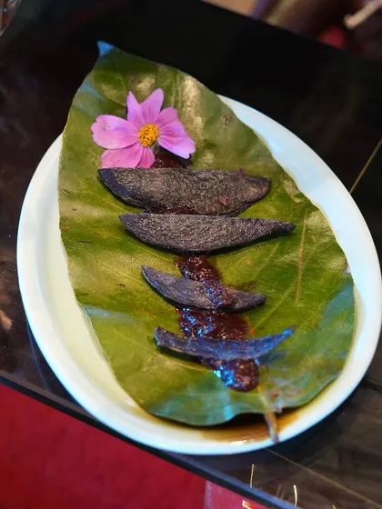 An artistic presentation of a unique dish featuring purple-hued elements on a bed of rich sauce, served on a natural leaf. This highlights our flair for creating visually intriguing and unconventional menu items.