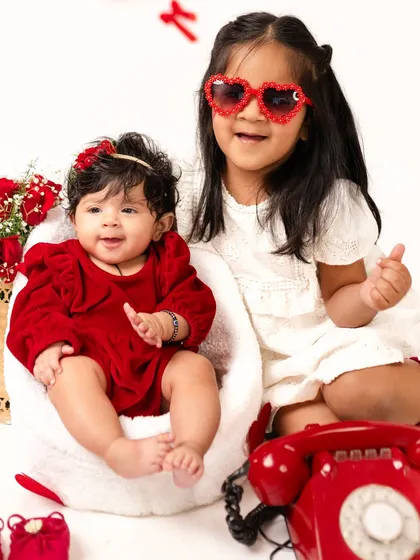 A Valentine's Day themed four-month milestone shoot with two sisters. The older sister's joy and the baby's sweet smile make this a perfect sibling portrait.