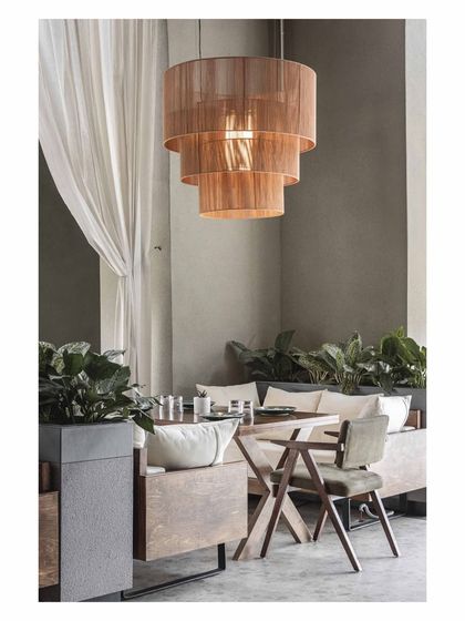 A detail shot of a lounge corner, showing the contrast between the rough texture of the planter and the soft cushions. The tiered pendant light adds a warm, sculptural element to this intimate setting.