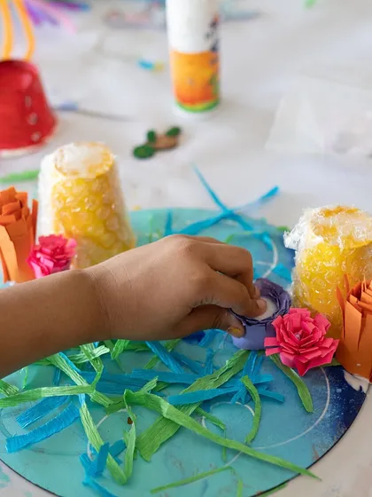 A close-up of a student working on a mixed-media diorama. They are adding paper grass and flowers to their underwater scene. These multi-step projects are great for teaching planning and patience.
