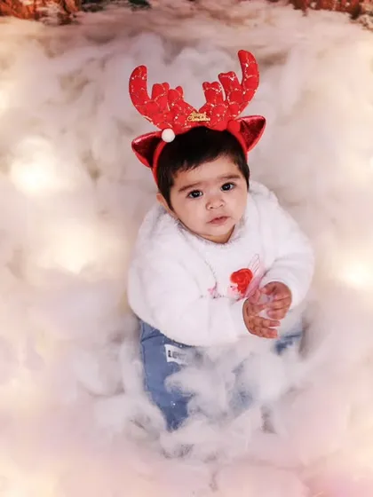 A baby with reindeer antlers sits in a magical, illuminated cloud of snow.