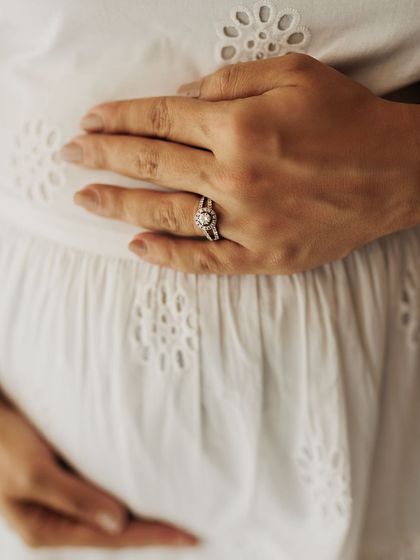 A close-up of the mother's hands on her belly, her wedding ring a symbol of the family's foundation. The delicate fabric of her dress adds beautiful texture.