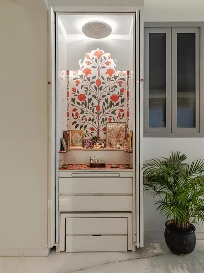 This compact pooja unit shows how a sacred space can be integrated seamlessly into a modern home. Featuring a beautiful tree-of-life wallpaper backdrop and a glossy white acrylic finish, the unit includes multiple drawers for storage and can be concealed with pocket doors, making it both beautiful and space-efficient.