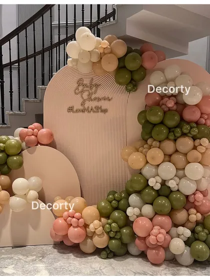 A modern and chic baby shower backdrop with an organic balloon garland in earthy tones of olive, pink, and beige.
