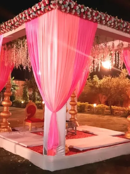A side view of a lovely pink-themed wedding mandap. The combination of drapes and hanging florals creates a romantic and festive atmosphere for an outdoor evening ceremony.