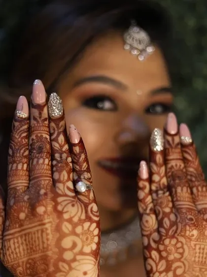 A beautiful bride showcasing her custom wedding nails, designed to complement her intricate henna. This set features a soft pink base with sparkling silver glitter accent nails.