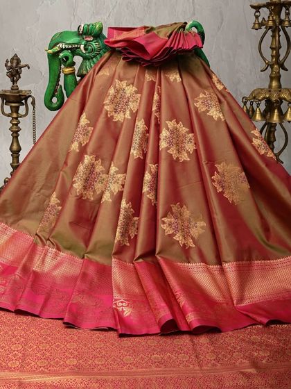 A dual-toned silk saree in shades of rust and olive green. The body is adorned with large, woven gold floral motifs, giving it a rich and festive appearance.