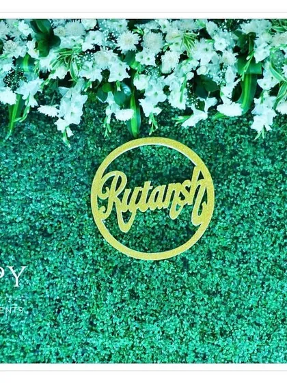 A close-up of the "Rutansh" name cutout against the lush green backdrop. We ensure every detail is perfect for your special day.