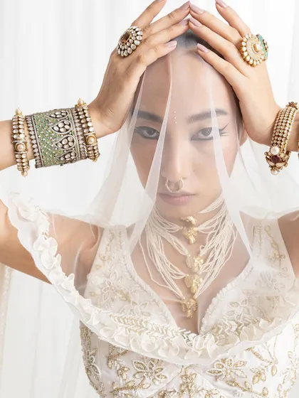 A powerful close-up from the "Rumi" campaign, where the styling is all about the accessories. The model is veiled, drawing all attention to the stacked polki bangles, statement rings, and the unique layered pearl and gold necklace.