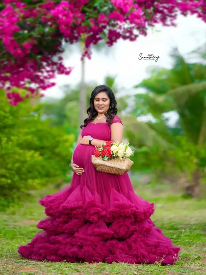 A beautiful outdoor portrait of a mother-to-be in a magenta gown, surrounded by flowers. The natural light and vibrant colors create a stunning and joyful image.