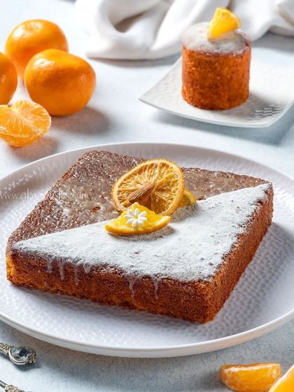 A square orange drizzle cake with a dual powdered sugar and glaze finish, showcasing a creative presentation for a bakery.