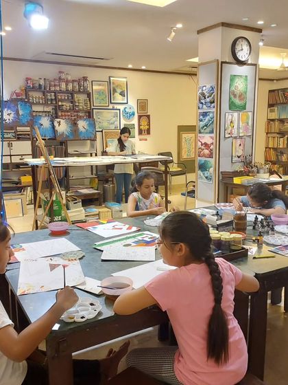 The studio is designed with different zones to accommodate various projects, from large canvas paintings on easels to detailed ink work at the tables.