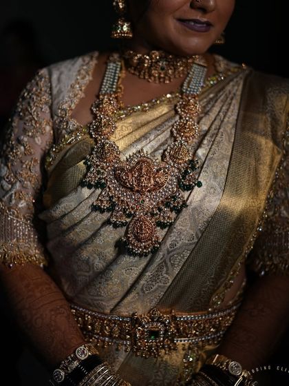 A close-up of a bride's torso, showing the intricate details of her temple jewelry and the embroidery on her blouse.