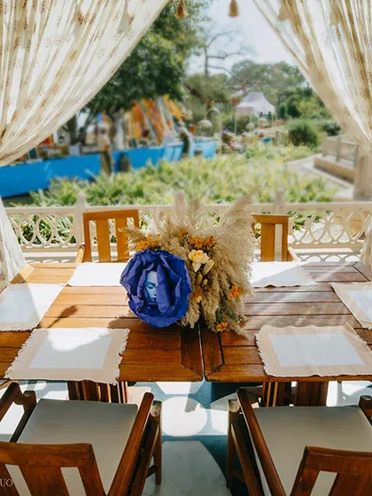 A tablescape that blends the rustic with the artistic. A pampas grass centerpiece is accented with a surreal blue rose containing a face, adding a touch of avant-garde magic.