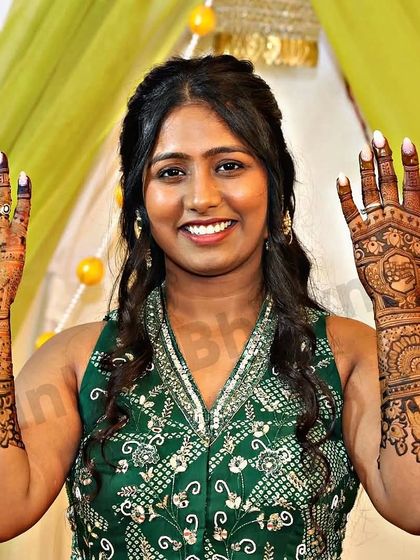 A smiling bride proudly displays her full bridal mehndi. The design includes personalized initials and a mix of traditional motifs, perfectly capturing her joy on her special day.