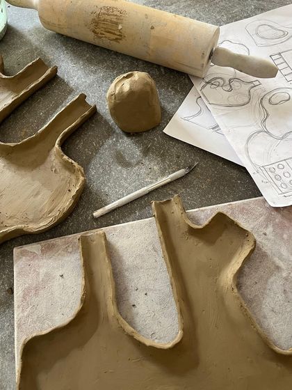 The initial stages of a hand-building project, with sketches, tools, and clay slabs ready to be assembled.
