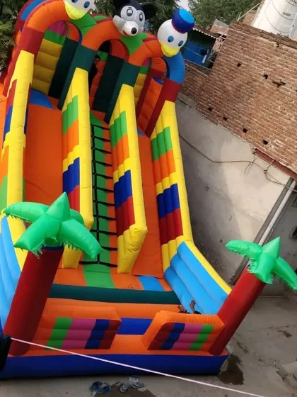 A high-angle view of a 3-slider bouncy with palm tree decorations, showing the slide and climbing areas.