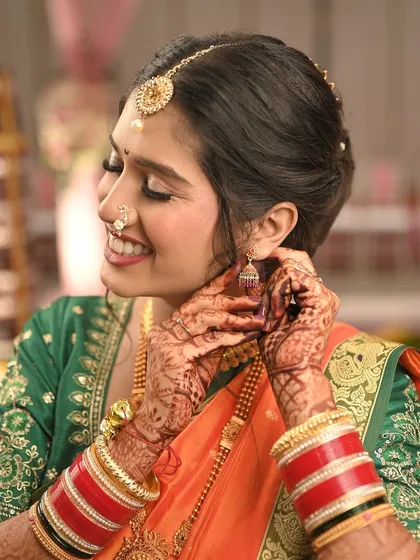 A close-up shot capturing the bride's joyful expression as she puts on her earring. This highlights the detailed eye makeup and her radiant skin.