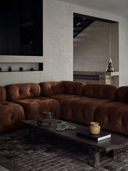 A full view of the plush, modular sofa that anchors the living room. The design prioritizes comfort and creates a warm, enveloping atmosphere for the family.