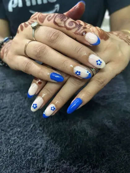 Adding a pop of color to a French manicure. This design features a vibrant blue French tip on an almond-shaped extension, with tiny, hand-painted white flowers for a cute, summery feel.