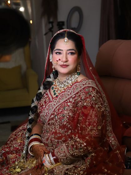 A full-length view of our beautiful bride in her red lehenga. The makeup is balanced to complement the heavy embroidery and jewelry, with a long, decorated braid.