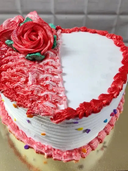 A heart-shaped cake with a half-and-half design. One side is smooth white, while the other has a textured red pattern and a buttercream rose.