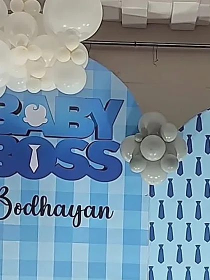 A detailed shot of the backdrop for a Baby Boss themed party. This image shows the custom 'Baby Boss' text, a checkered and tie-patterned background, and the intricate balloon work in shades of blue, white, and grey.