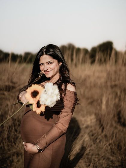 A lovely portrait of the mom-to-be in a golden field, offering a bouquet of sunflowers to the camera with a sweet smile.