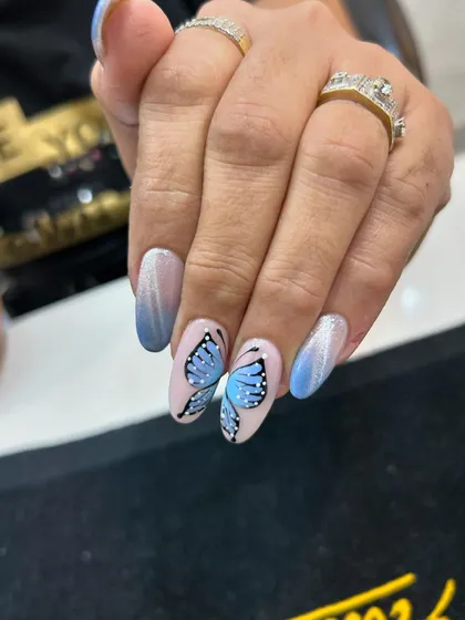 Let your nails take flight with our custom hand-painted butterfly art. This detailed design is set against a beautiful blue ombré and cat eye background, showing the delicate and artistic work our nail technicians are capable of.