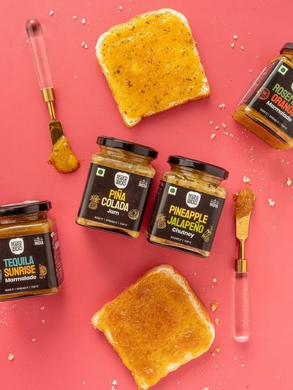 A playful flatlay showing different jams and marmalades on toast. This image demonstrates the product in use, making it relatable and inspiring for customers. The bright pink background is fun and grabs attention.