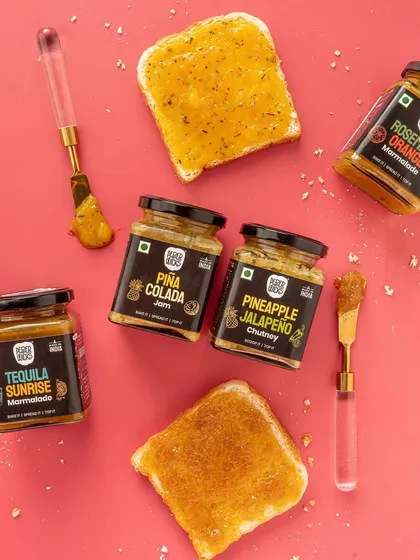 A playful flatlay showing different jams and marmalades on toast. This image demonstrates the product in use, making it relatable and inspiring for customers. The bright pink background is fun and grabs attention.
