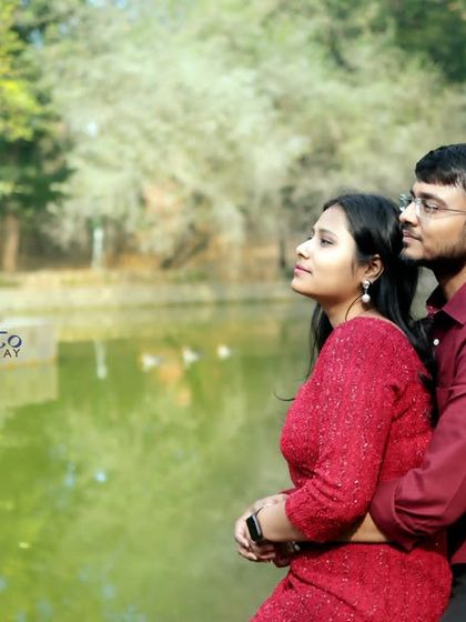 A romantic embrace by the lake, capturing a candid moment as the couple looks out at the view. The natural daylight and green backdrop make for a beautiful outdoor couple photo.