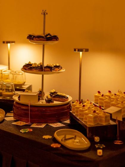 A warmly lit dessert station creates an inviting and indulgent atmosphere. The multi-tiered stands and glowing lamps highlight the decadent array of sweet treats available for guests.