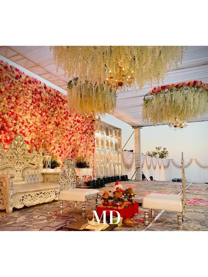 A close up of the seating on a grand wedding stage. The ornate, throne-like chairs are placed against a massive wall of flowers, ensuring the couple is the center of attention in a truly regal setting.