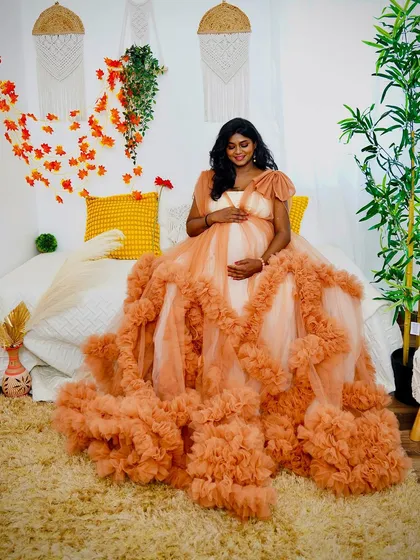 The full splendor of our peach ruffled gown is on display in this shot. The client is seated in our boho bedroom setup, with the long trail of the dress creating a stunning visual.