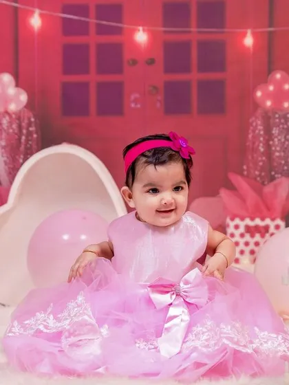 The birthday girl looking adorable in her pink dress, seated in front of the charming pink dollhouse backdrop.