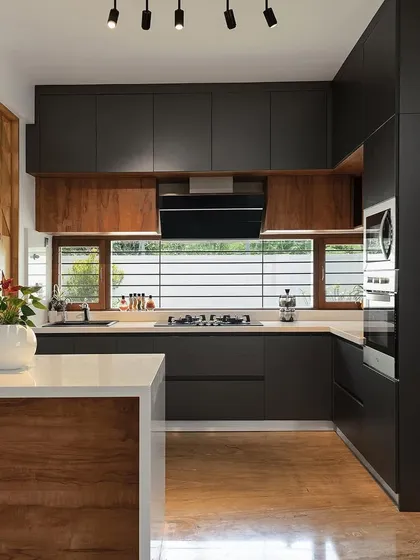 Our award-winning kitchen designs focus on clean lines, smart functionality, and natural light. This kitchen from the Cube House project uses a contrasting palette of dark laminates and warm wood, with an open layout and large window to create an efficient and inviting cooking space.