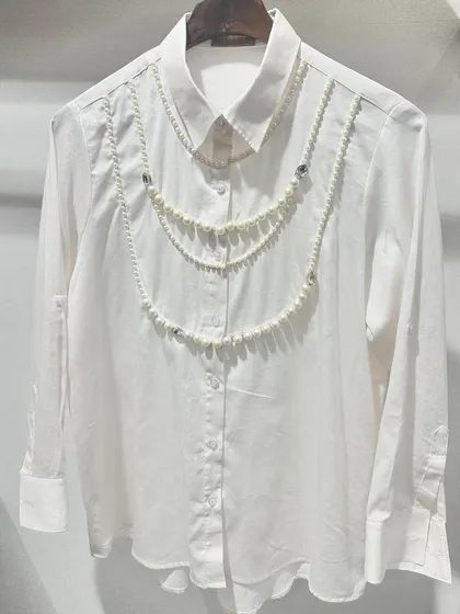 It's all in the details. This classic white shirt is crafted from opulent Swiss cotton and elevated with delicate, hand-draped pearl embellishments, turning a wardrobe staple into a statement piece for lunches or evening events.