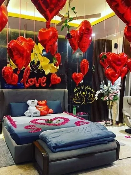 A luxurious 'LOVE' themed room decoration with red heart-shaped foil balloons and rose petals on the bed.