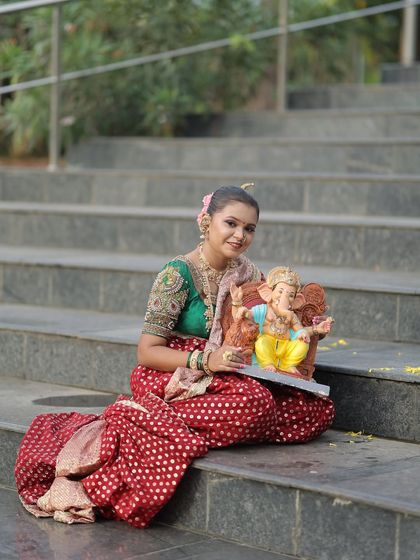 Seated on the steps with a Ganpati idol, this image shows the full drape of the red dotted Nauvari.