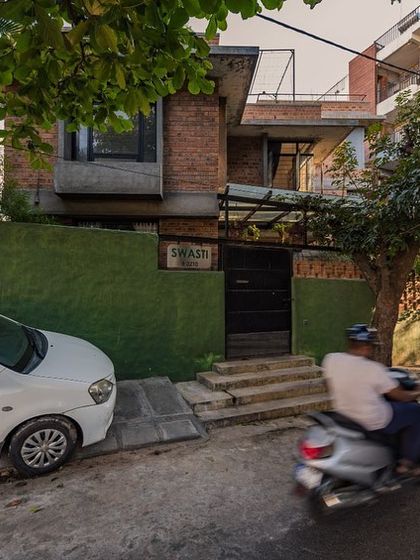 The street view of Roopasri's home, "Swasti," which blends into its green surroundings. The design prioritizes privacy while maintaining a connection to the neighborhood.