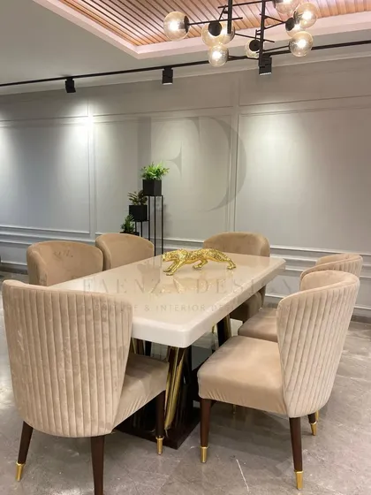 A modern dining set with a white onyx top table and a sculptural gold and dark wood base. The chairs are upholstered in a pleated beige velvet, creating a light and sophisticated dining area.