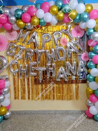 A colorful birthday decoration with a silver and gold balloon arch and a gold fringe backdrop.