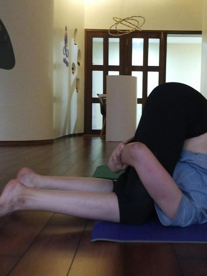 A student practices Karnapidasana (Ear Pressure Pose), an advanced inversion that deeply stretches the spine and calms the nervous system.