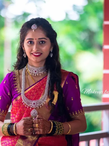 This is a perfect example of a modern reception look. The client is wearing a vibrant pink and purple Kanjeevaram saree with elegant diamond jewelry. Her makeup is glamorous yet sophisticated, with soft, flowing curls completing the style.