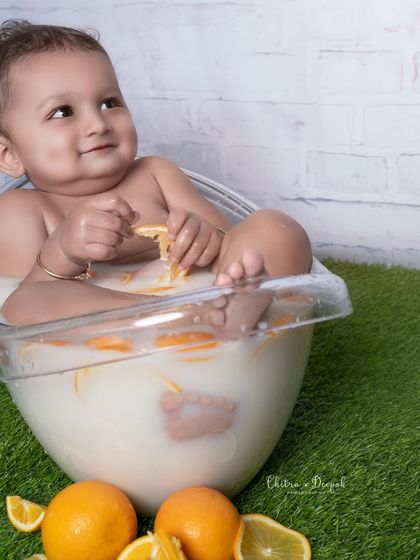 A sweet, contemplative moment as the baby boy plays with an orange slice during his fun and sensory milk bath photoshoot.