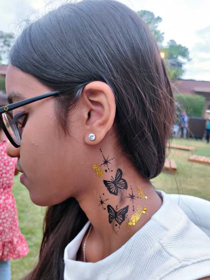 A temporary tattoo of two butterflies on the neck, accented with gold glitter stars.