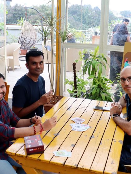 Three friends enjoying a card game on a sunny afternoon. Our bright yellow table is the perfect spot for some lighthearted fun.
