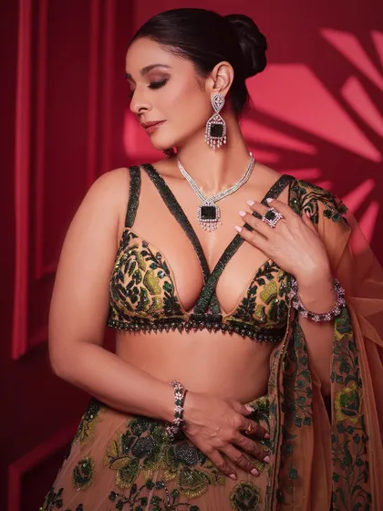 A close-up on the exquisite details of the blouse and the stunning emerald and diamond jewelry. The makeup is kept sophisticated to complement the intricate outfit.